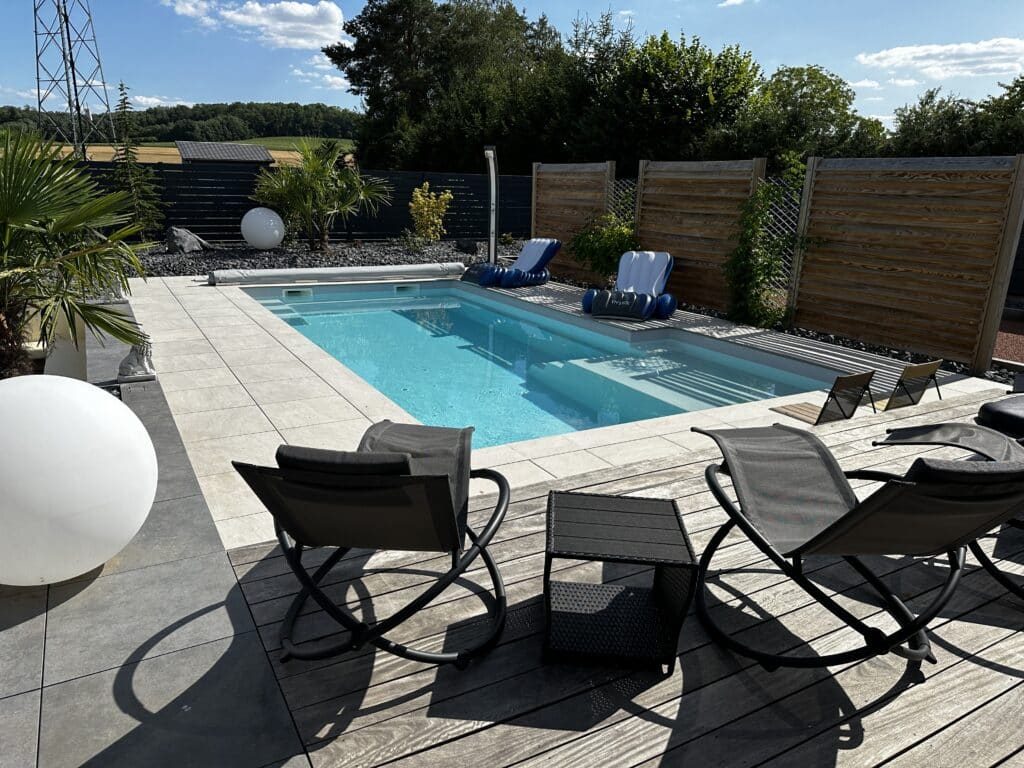 Piscine à coque avec plage en dalles et terrasse bois, réalisée par A2E Paysages